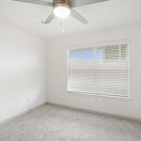 A room with a ceiling fan and a window with blinds.